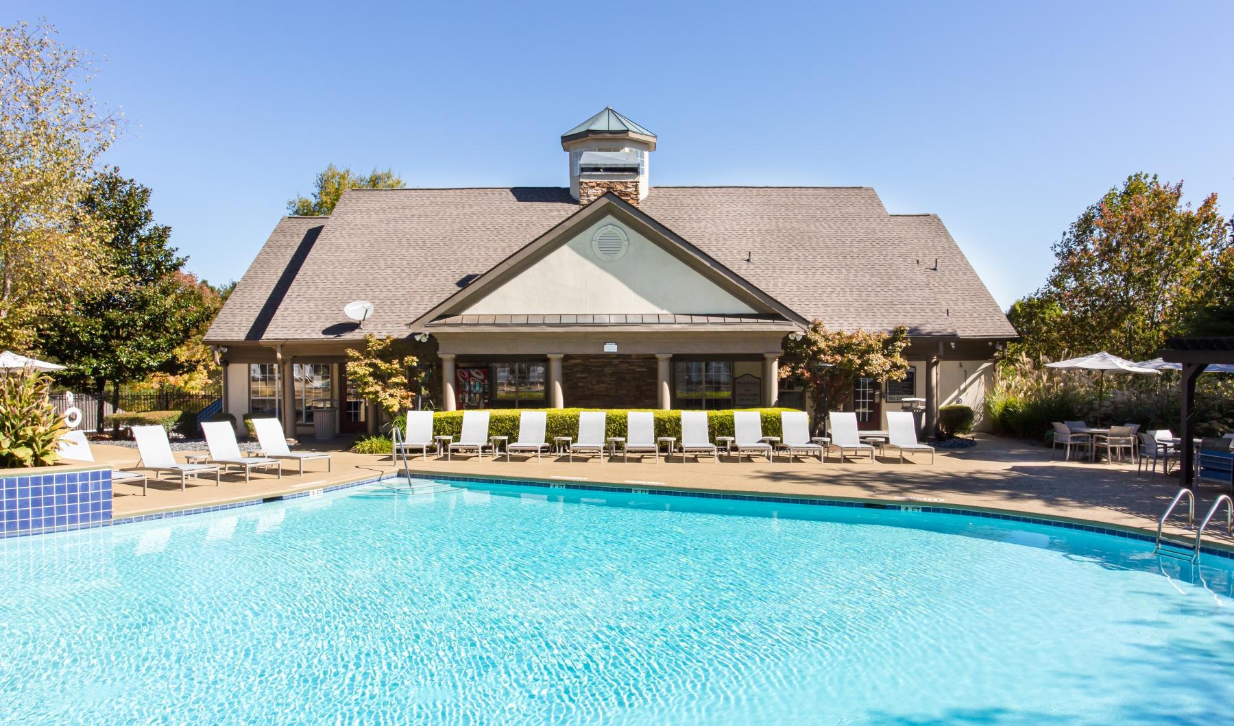 a swimming pool with chairs and umbrellas in front of a house